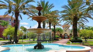 A multi-tiered fountain surrounded by palm trees and a building with arched windows.