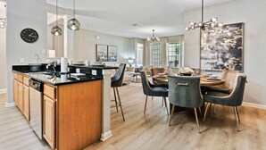 A modern kitchen with a central island, dining area with chairs, and a chandelier.