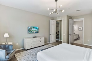 A bedroom with a bed, a dresser, a television, and a door leading to another room. - Fantastic balcony view 3BR near Epic Universe! (Orlando)