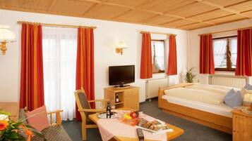 Habitación de hotel con techo de madera, una cama, un televisor, un escritorio con control remoto y una mesa de comedor con una revista y fruta.