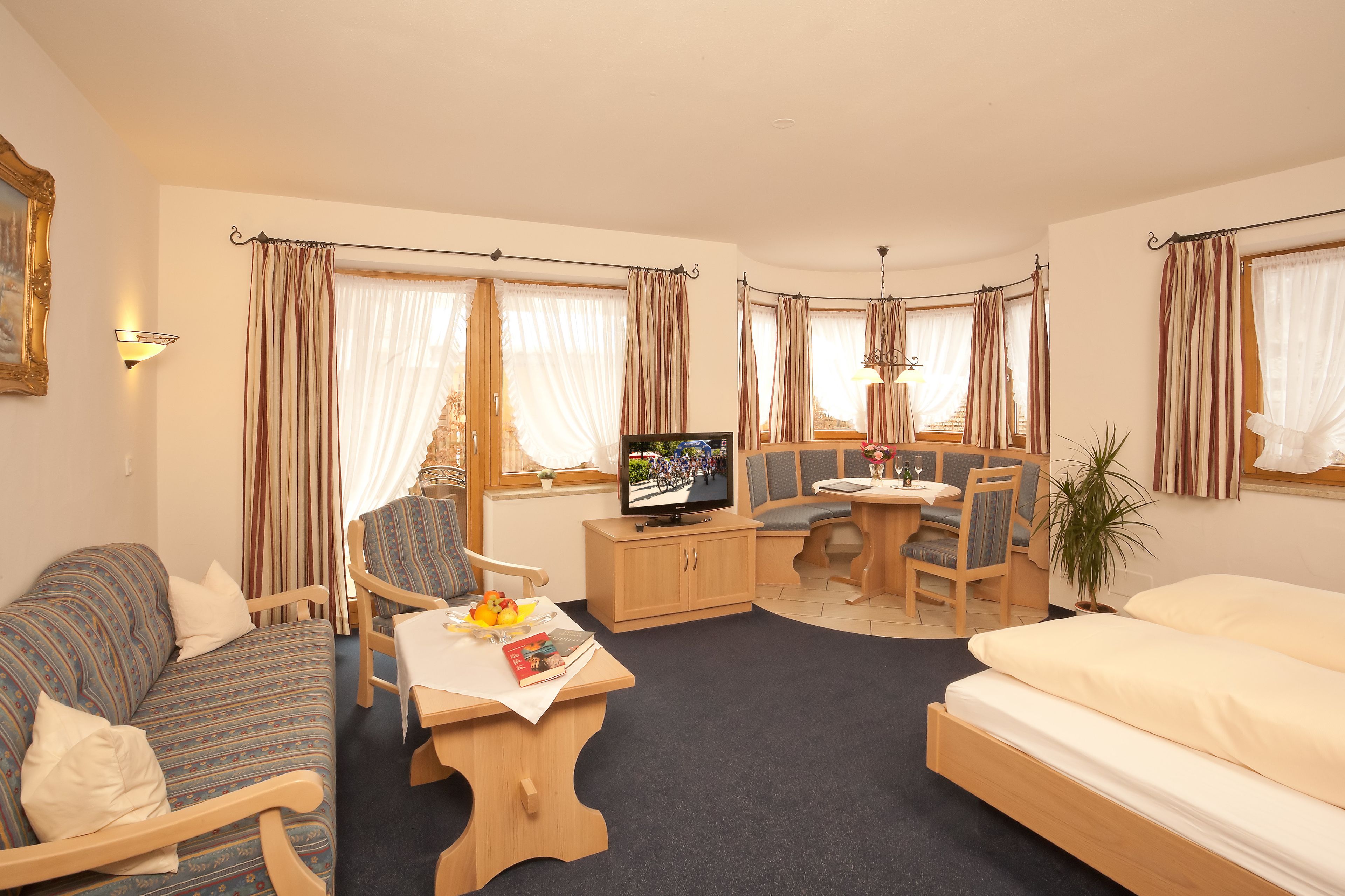 Une chambre d’hôtel avec un canapé, une table à manger et des chaises, un téléviseur, un lit et une plante en pot.