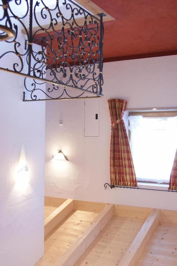 Ein Zimmer mit einer Holztreppe, einem Fenster mit Vorhängen und einem dekorativen Metallgeländer.