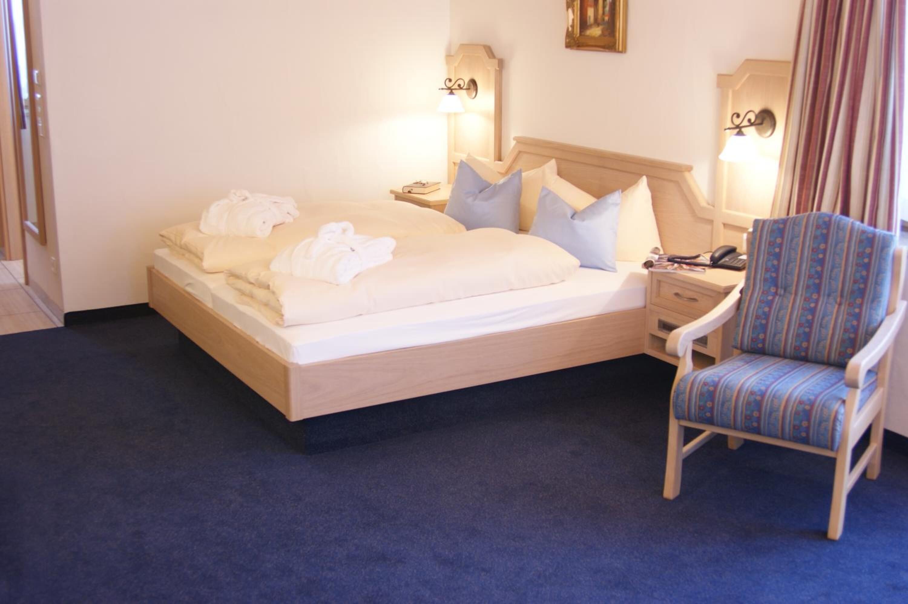 A hotel room with a bed, a chair, and a nightstand with a lamp.