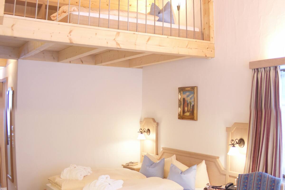 Een slaapkamer met een stapelbed, een enkel bed, een stoel en een nachtkastje met een lamp.