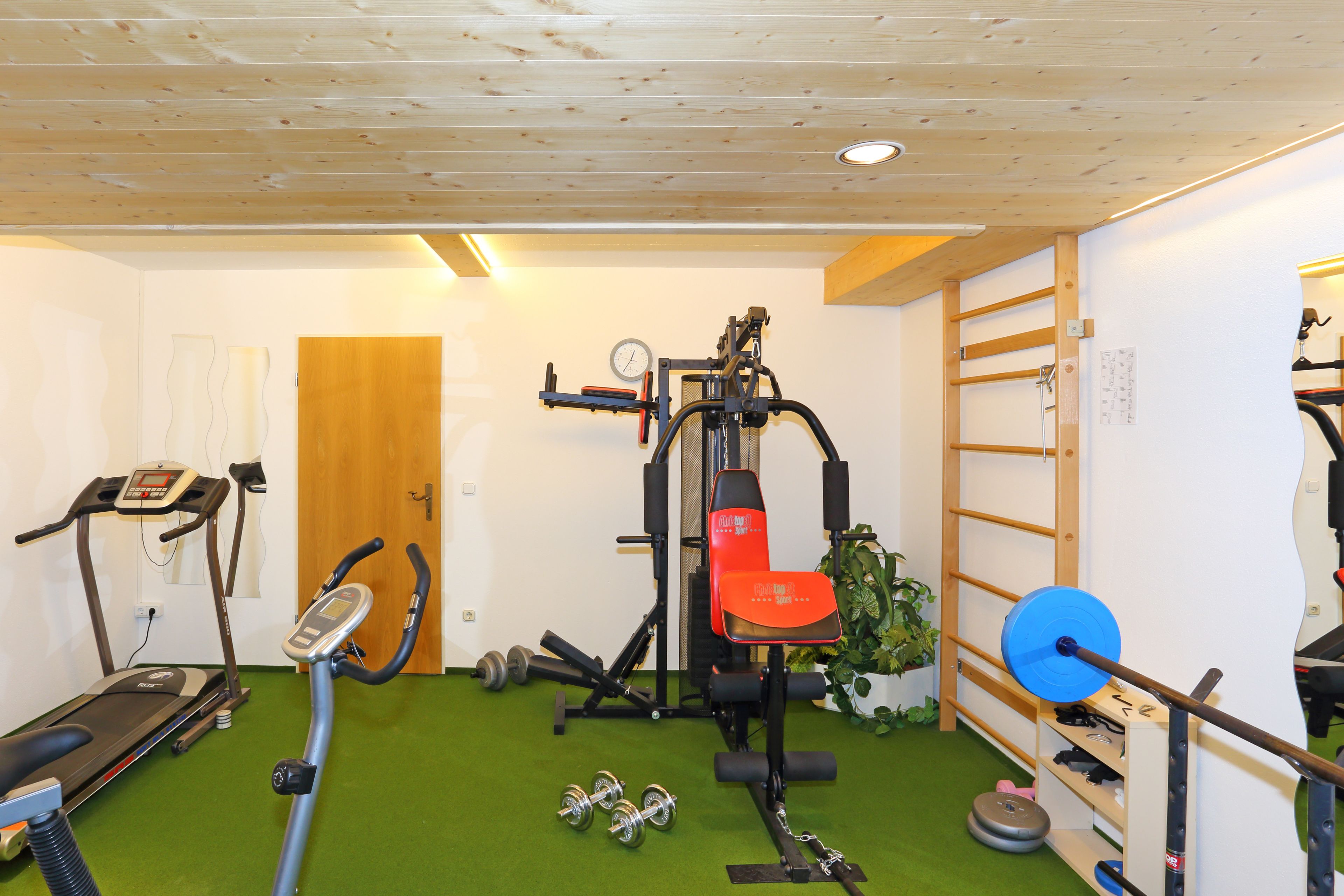 Un gimnasio con equipo de ejercicio, incluyendo una cinta de correr, un banco de pesas y mancuernas.