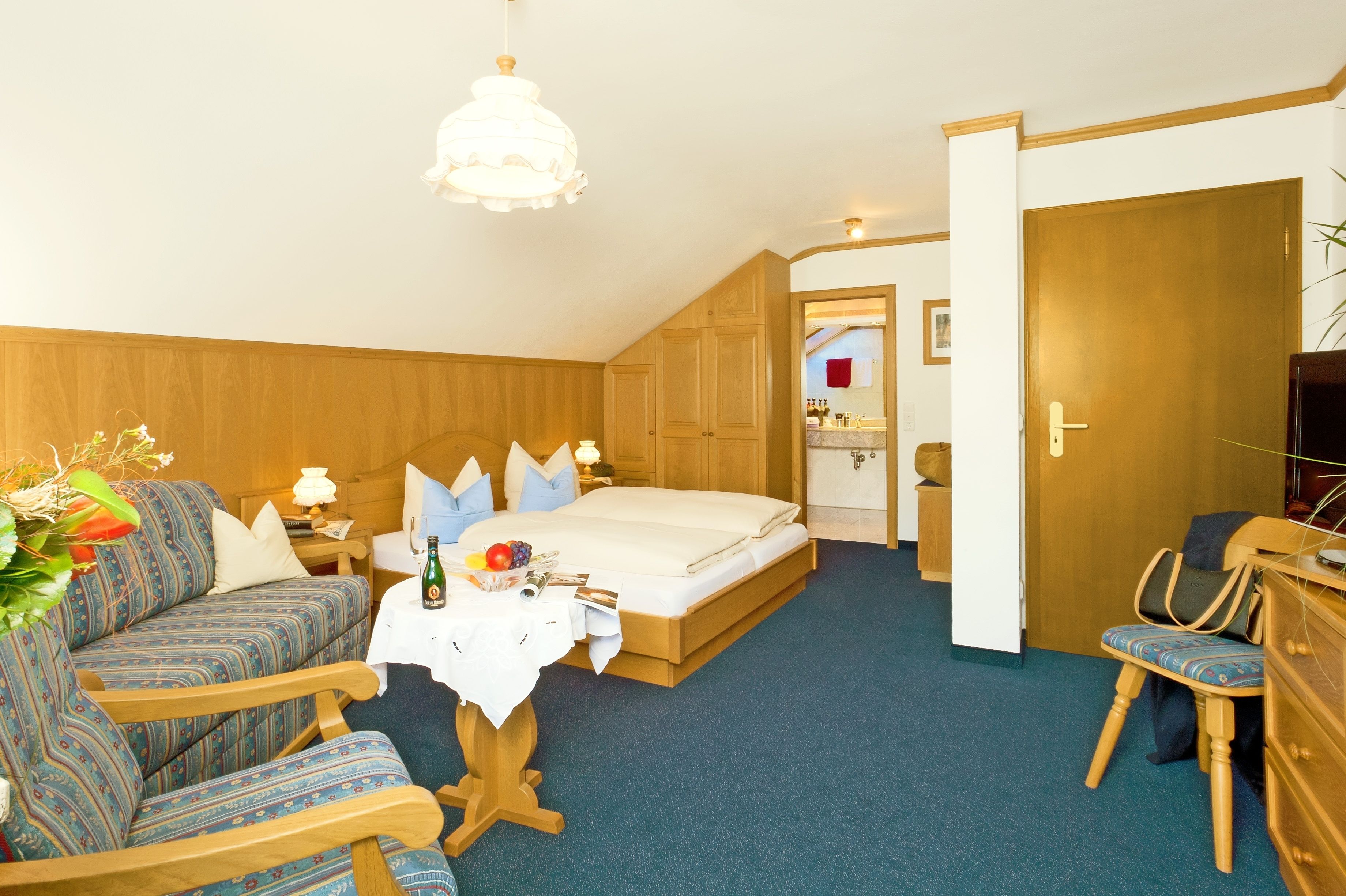 A cozy hotel room with a bed, a sofa, a small table with a bottle and fruit, and a television.