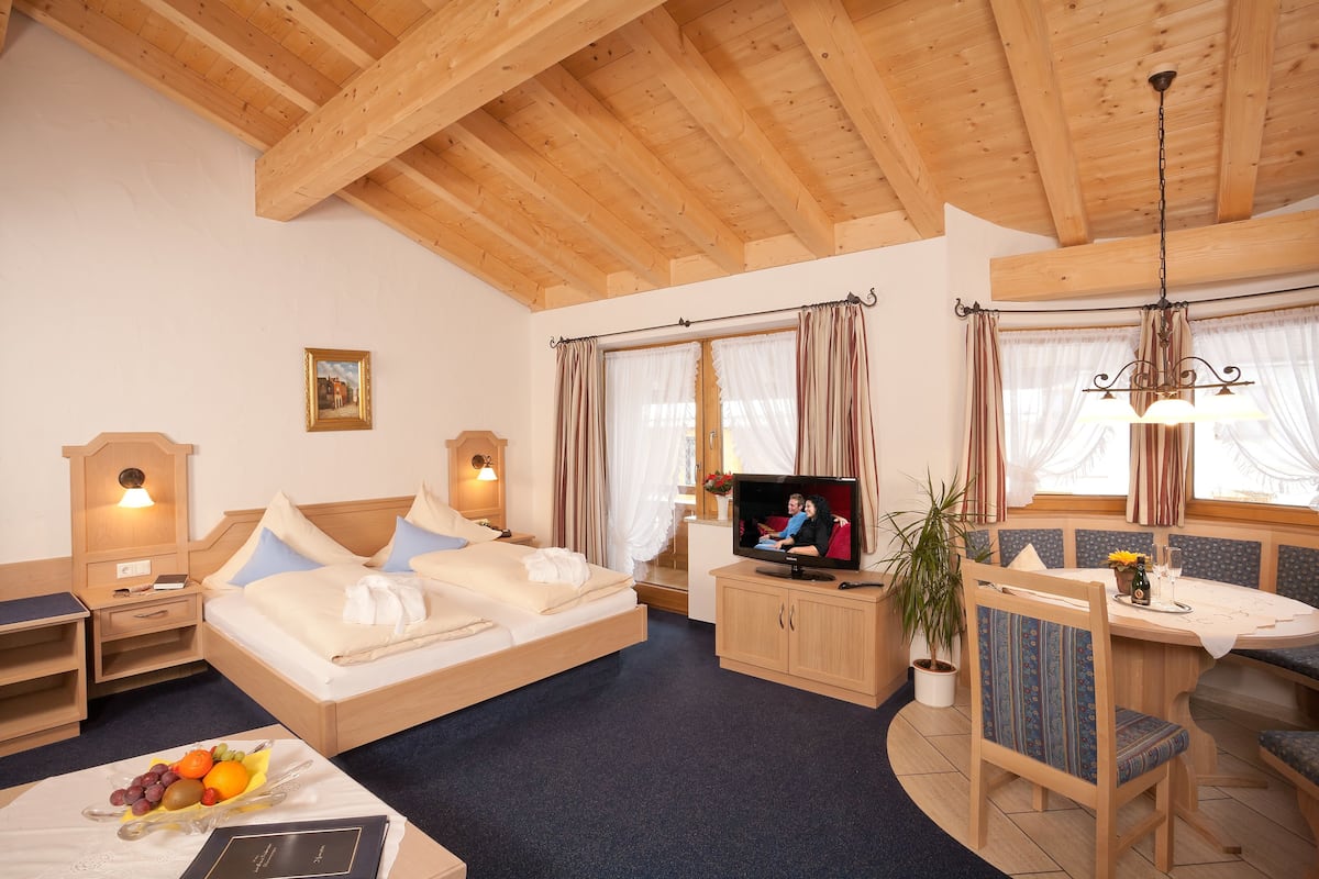 Een knus hotelkamer met een bed, een televisie, een zithoek met een tafel en stoelen, en een kamerplant.