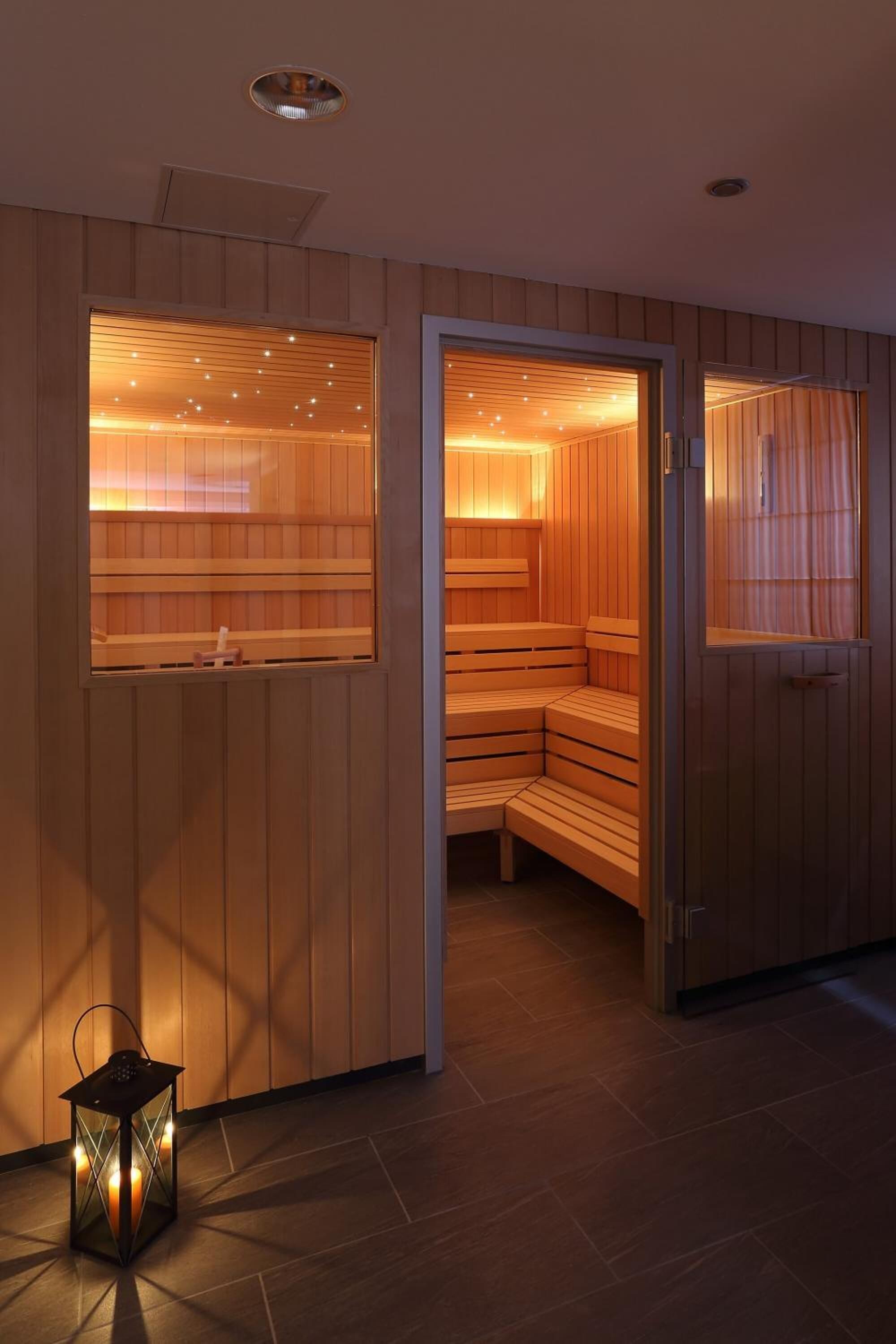 Un cuarto de sauna con bancos de madera, una puerta de cristal, una mesita y un farol en el suelo.