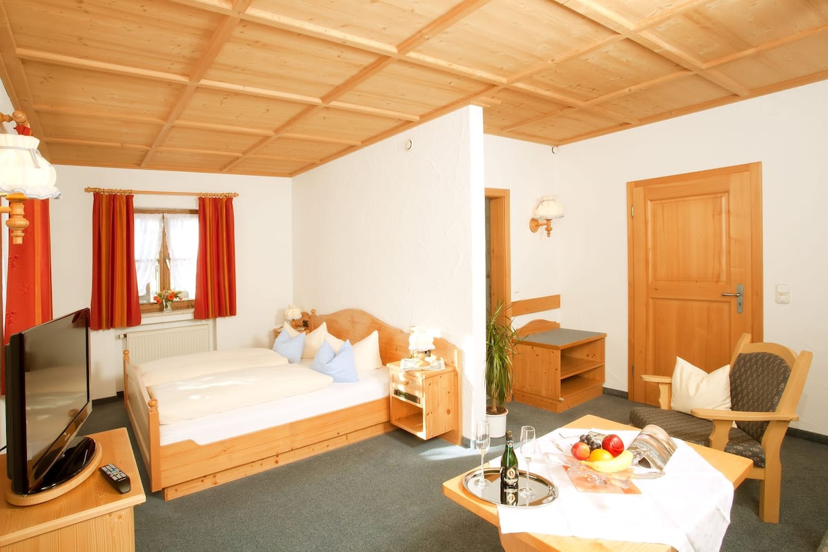 Een gezellige kamer met een bed, nachtkastje, televisie en een eethoek met een schaal fruit en een fles.