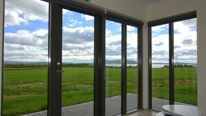 Una habitación con grandes puertas de vidrio que dan a un campo cubierto de césped y un lago, una mesita pequeña y un control remoto sobre ella.
