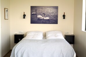 A bedroom with a bed, two bedside tables, and a wall-mounted picture of swans.
