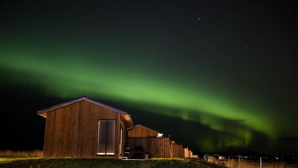 Un edificio de madera con un gran puerta y ventanas, ubicado en una colina cubierta de hierba con vista al cielo nocturno.