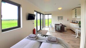 Un dormitorio moderno con un ventanal grande, un televisor de pantalla plana y una kitchenette al fondo.