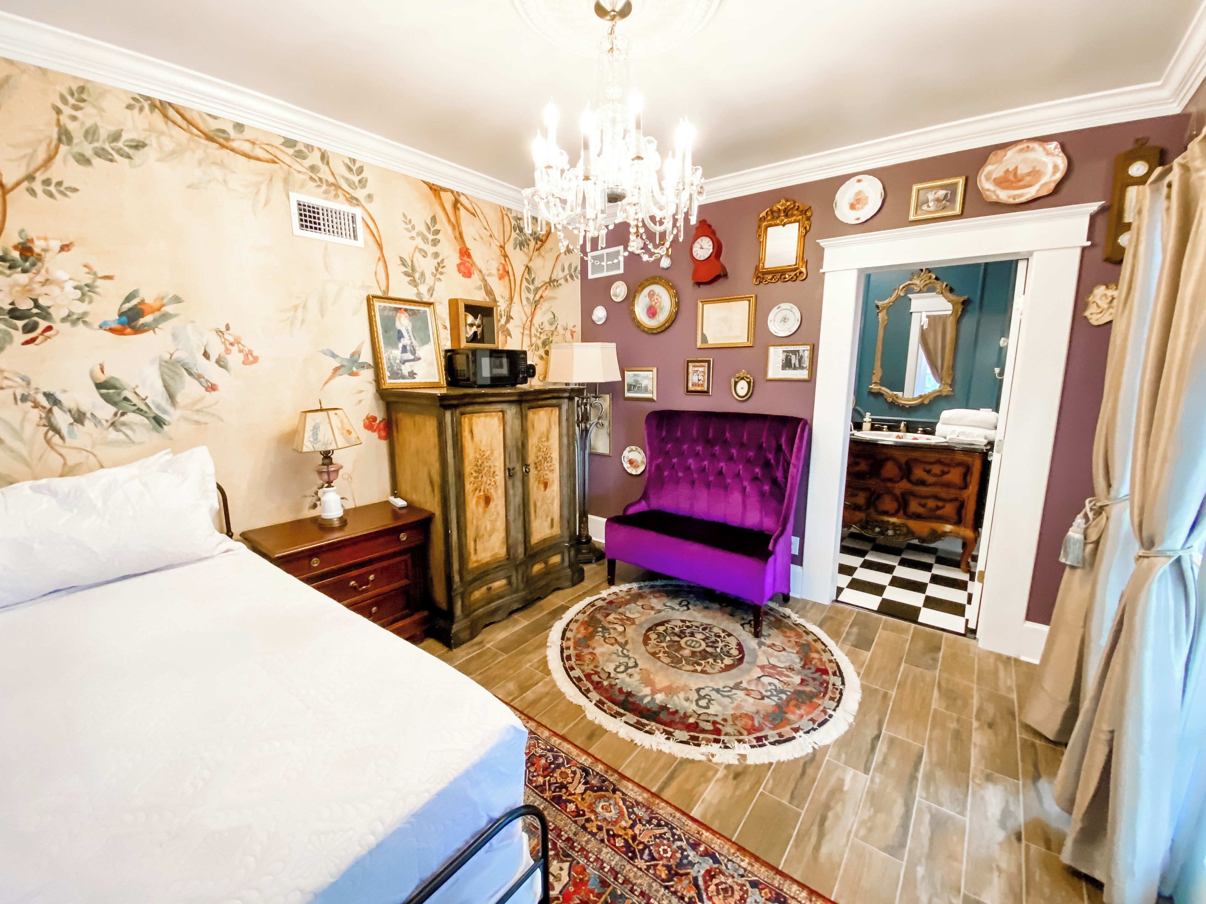 A bedroom with a bed, a purple armchair, a chandelier, and a checkered floor.