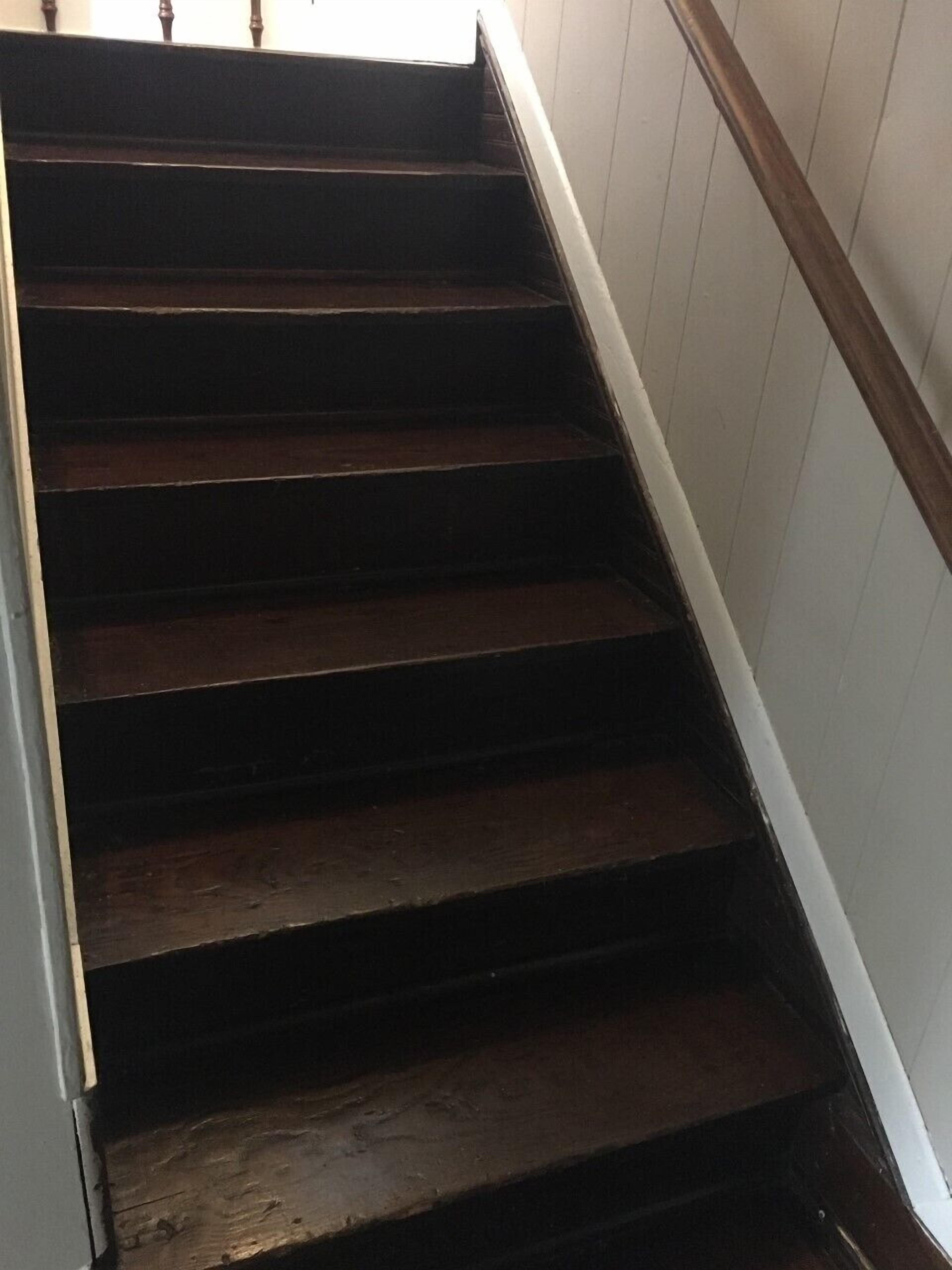 Een houten trap met een witte leuning en een donkere vloer.