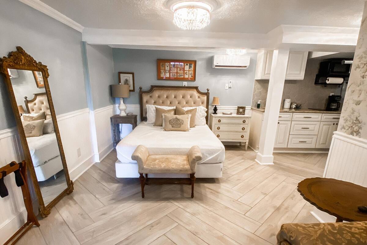 A bedroom with a large bed, a nightstand, a dresser, a mirror, and a chandelier.