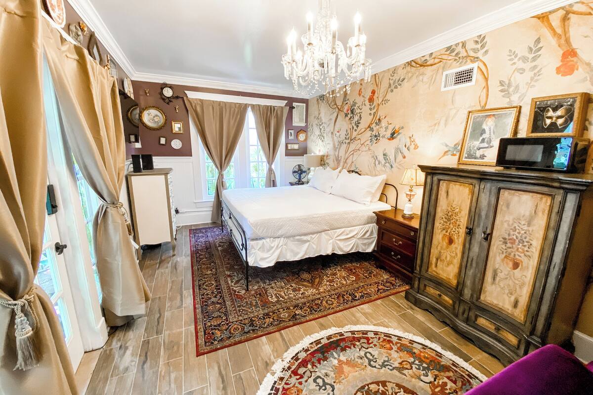 A bedroom with a large bed, a chandelier, a wooden cabinet, and a floral wallpaper design.