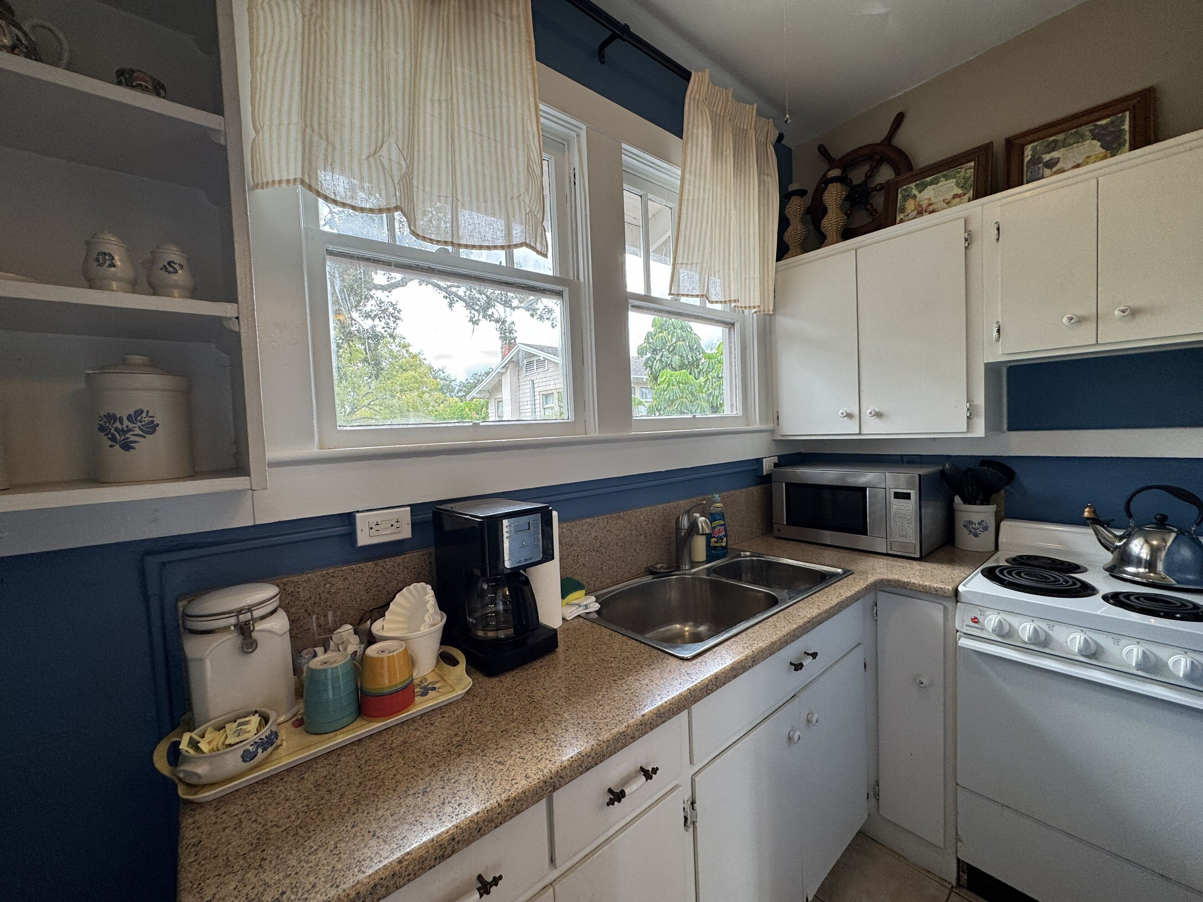 A kitchen with white cabinets, a microwave, a stove, a sink, and a window with curtains.