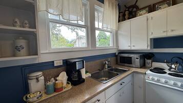 A kitchen with white cabinets, a microwave, a stove, a sink, and a window with curtains.