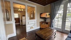 A spacious living room with a wooden coffee table, a wicker sofa, and a television mounted on the wall. - Park Place Inn and Cottages (Sanford)