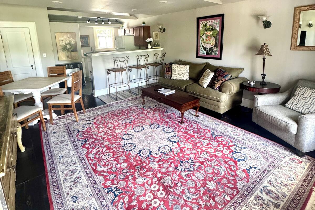A spacious living room with a large red and white patterned rug, a sofa, a coffee table, and a dining area with a wooden table and chairs.