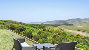 Une terrasse avec deux chaises et une table, d’où l’on peut admirer un paysage luxuriant composé de collines et d’une côte lointaine.
