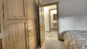 Ein Schlafzimmer mit Holzschrank, einem Bett mit gemusterten Betttextilien und einem Badezimmer mit Waschbecken und Spiegel.