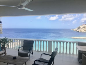A balcony with a view of the sea, white balustrades, and two chairs.