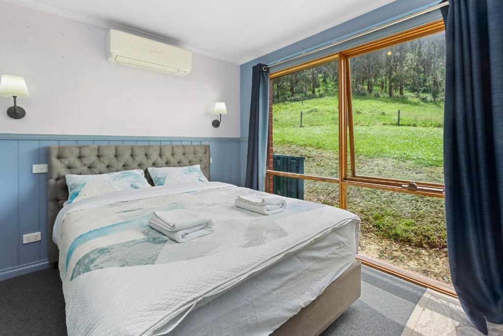 Une chambre à coucher avec un grand lit, deux lampes de chevet et une vue sur un espace verdoyant par la fenêtre.