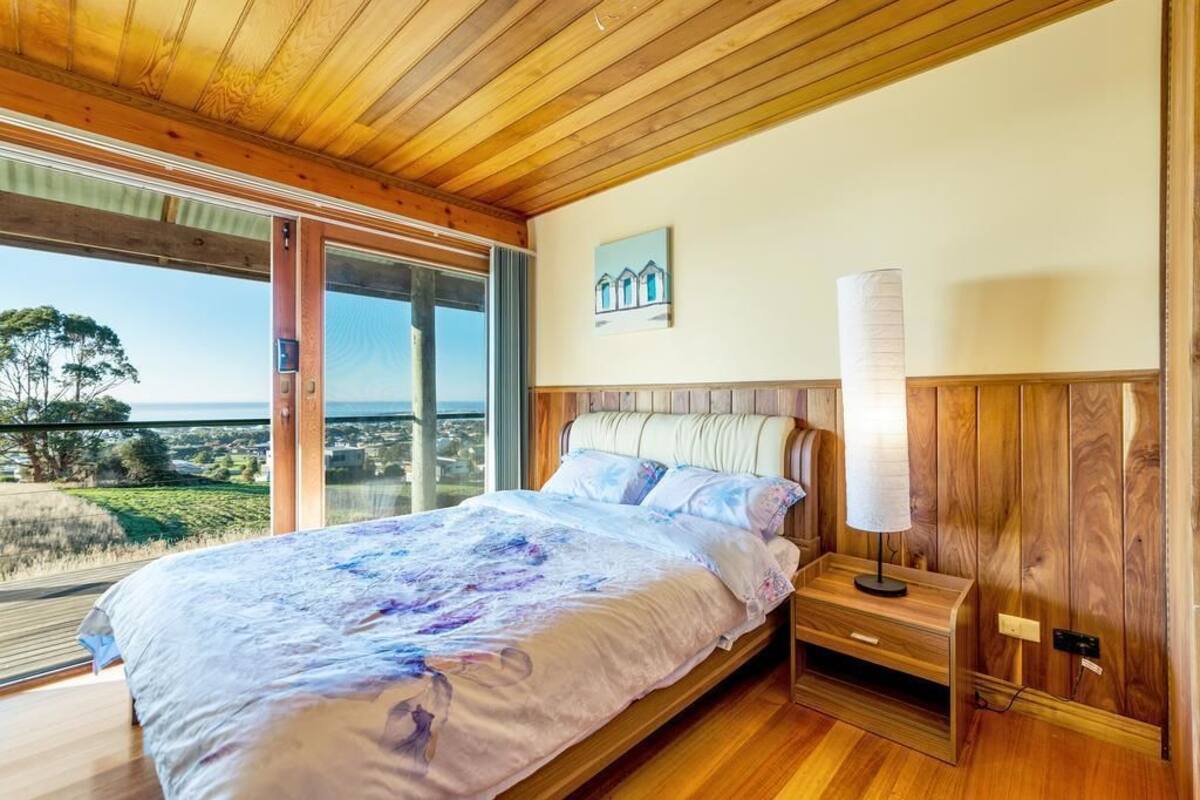 A bedroom with a large bed, wooden headboard, bedside table, and a view of the outdoors.