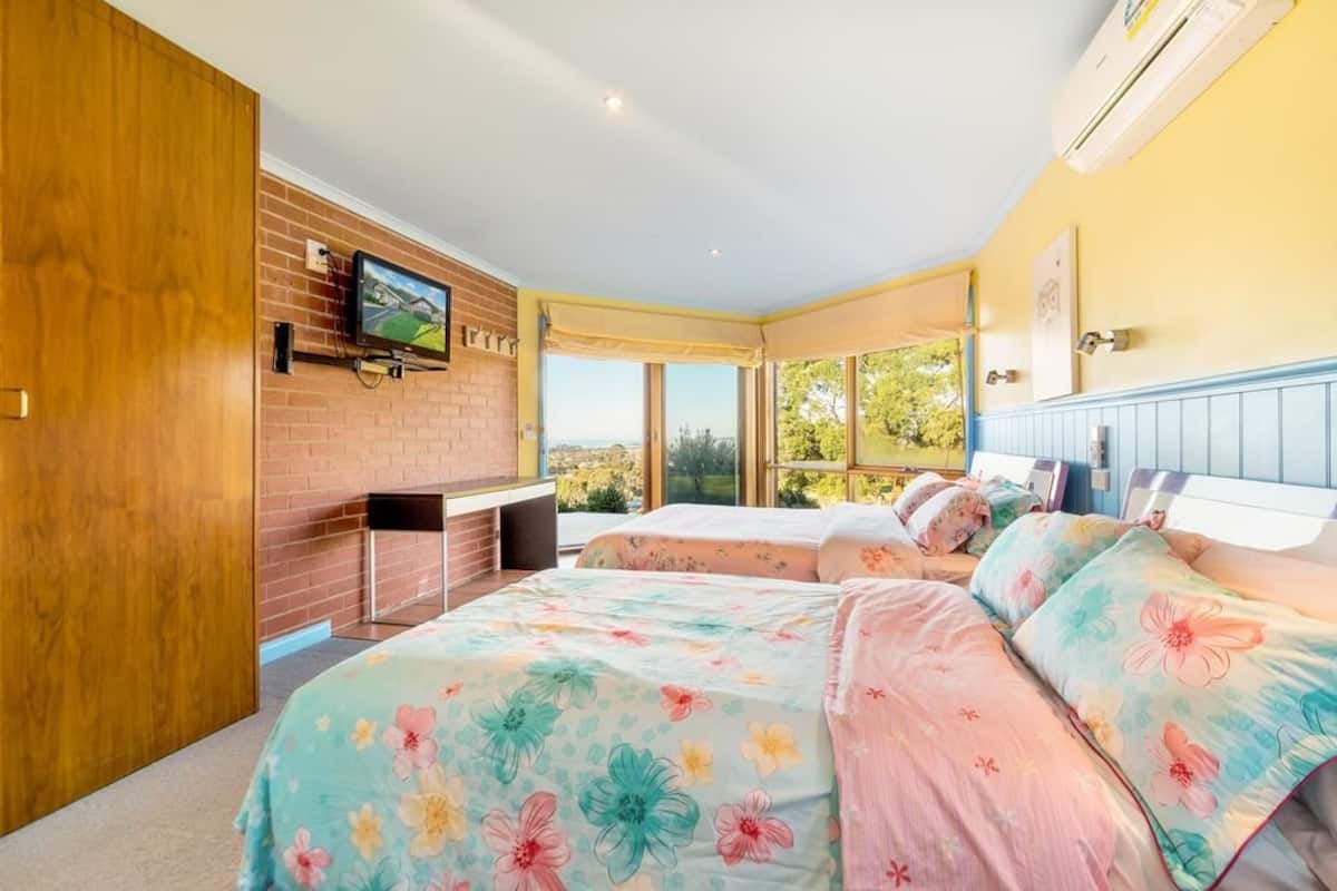 A bedroom with a large bed, a TV mounted on a brick wall, and a view of the outdoors.