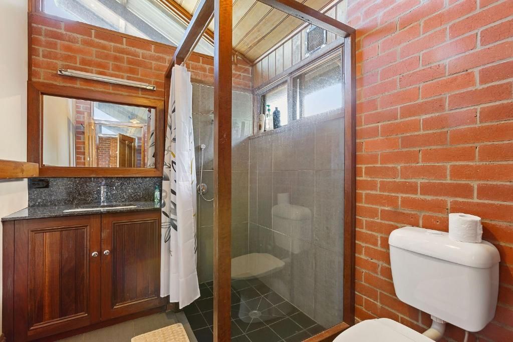 A bathroom with a shower enclosure, a toilet, and a wooden vanity with a mirror.