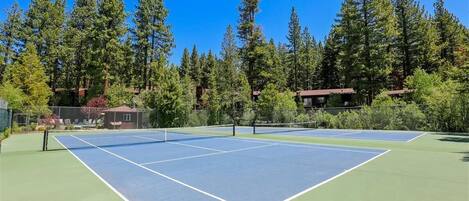 An outdoor tennis court surrounded by tall trees and a small building.