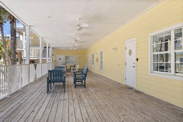 A covered outdoor area with wooden flooring, white railings, and ceiling fans.