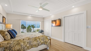 A bedroom with a bed, ceiling fan, window with view, and a TV on the wall. - Island House Beach Resort 13S (Siesta Key)
