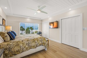Un dormitorio con cama, ventilador de techo, ventana con vistas y televisor en la pared.