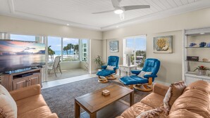 A spacious living room with a flat-screen TV, comfortable seating, a ceiling fan, and a view of the outdoors. - Island House Beach Resort 13S (Siesta Key)