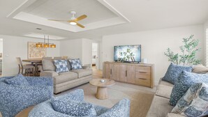 Ein modernes Wohnzimmer mit hoher Decke, Deckenventilator, Couchtisch aus Holz und Fernseher auf einer Holzkommode.