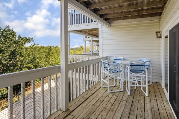 A covered porch with a wooden deck, white railings, and a table with blue and white chairs.