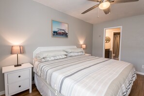 A bedroom with a bed, nightstands, a ceiling fan, and a door leading to a bathroom.