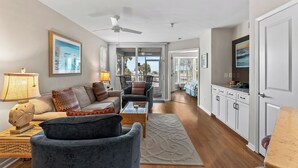 A spacious living area with a sofa, armchairs, a coffee table, and a TV. There is a ceiling fan, a window with a view, and a door leading to another room. - Fantastic Gulf View Villa with Resort Amenity Access! B3312A (Englewood)