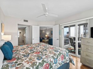 Quarto com cama, ventoinha no teto e vista para uma varanda com mobiliário exterior.
