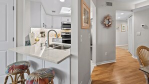 A modern kitchen with white cabinetry, a stainless steel sink, and a microwave. There are two wicker chairs with colorful cushions. - Fantastic Gulf View Villa with Resort Amenity Access! B3312A (Englewood)