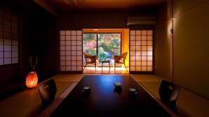 A traditional Japanese room with tatami flooring, a low table with a tea set, and sliding doors leading to a garden with colorful foliage. - Kogane Sansou (Nakatsu)