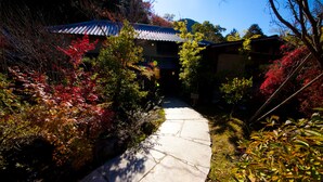 A traditional Japanese garden with a stone pathway leading to a building with a tiled roof. - Kogane Sansou (Nakatsu)