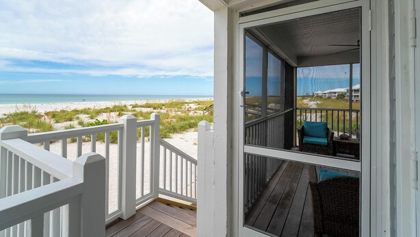 Eine überdachte Veranda mit Blick auf den Strand, einem weißen Geländer und einem Korbstuhl.