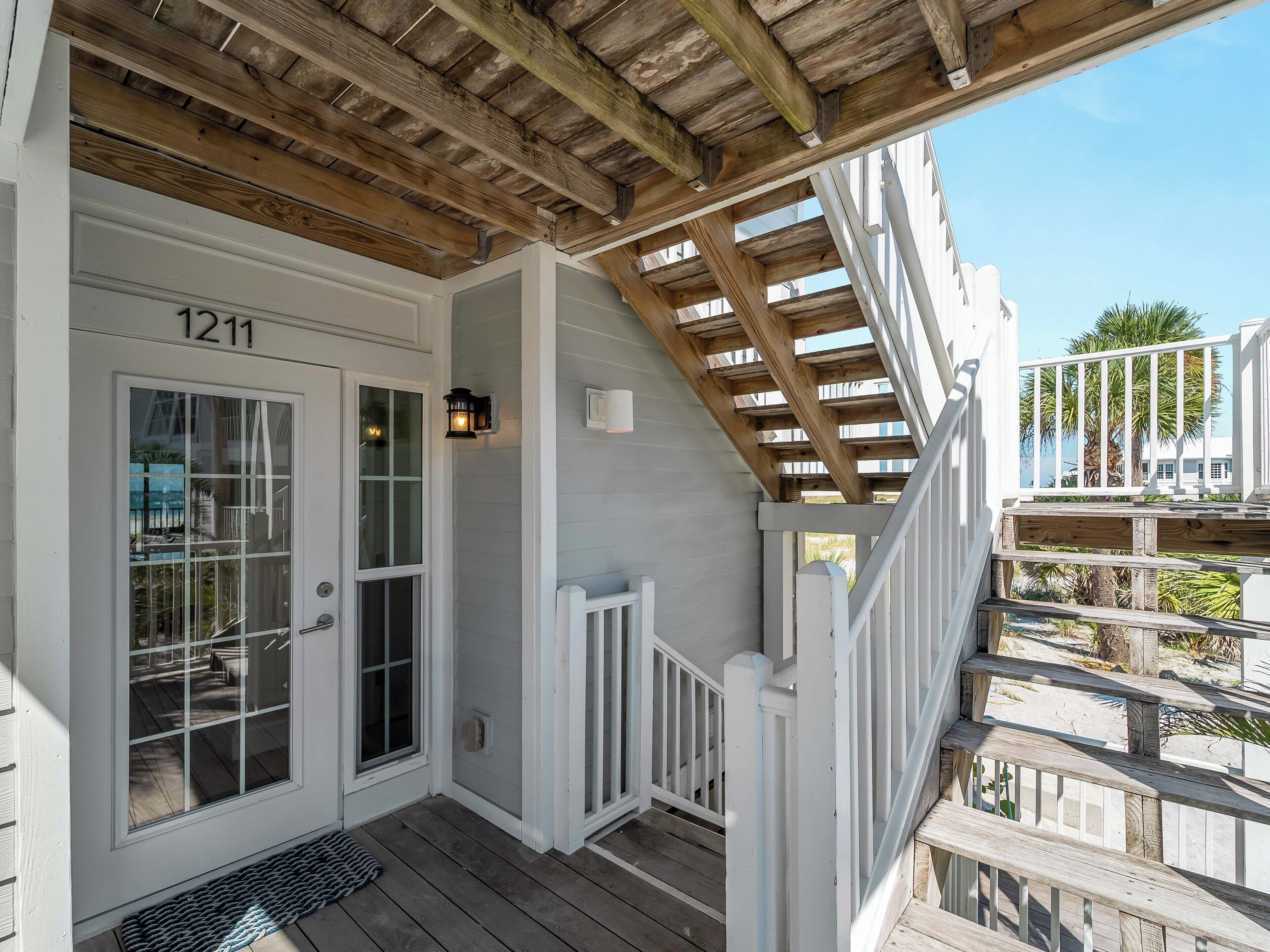A wooden deck with a white railing, a door labeled "1211", and a small porch area with a bench.