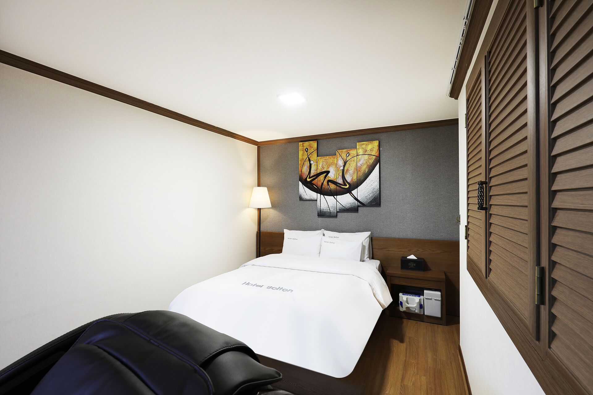 Una habitación de hotel con una cama, una mesita de noche, una lámpara y una obra de arte en la pared.