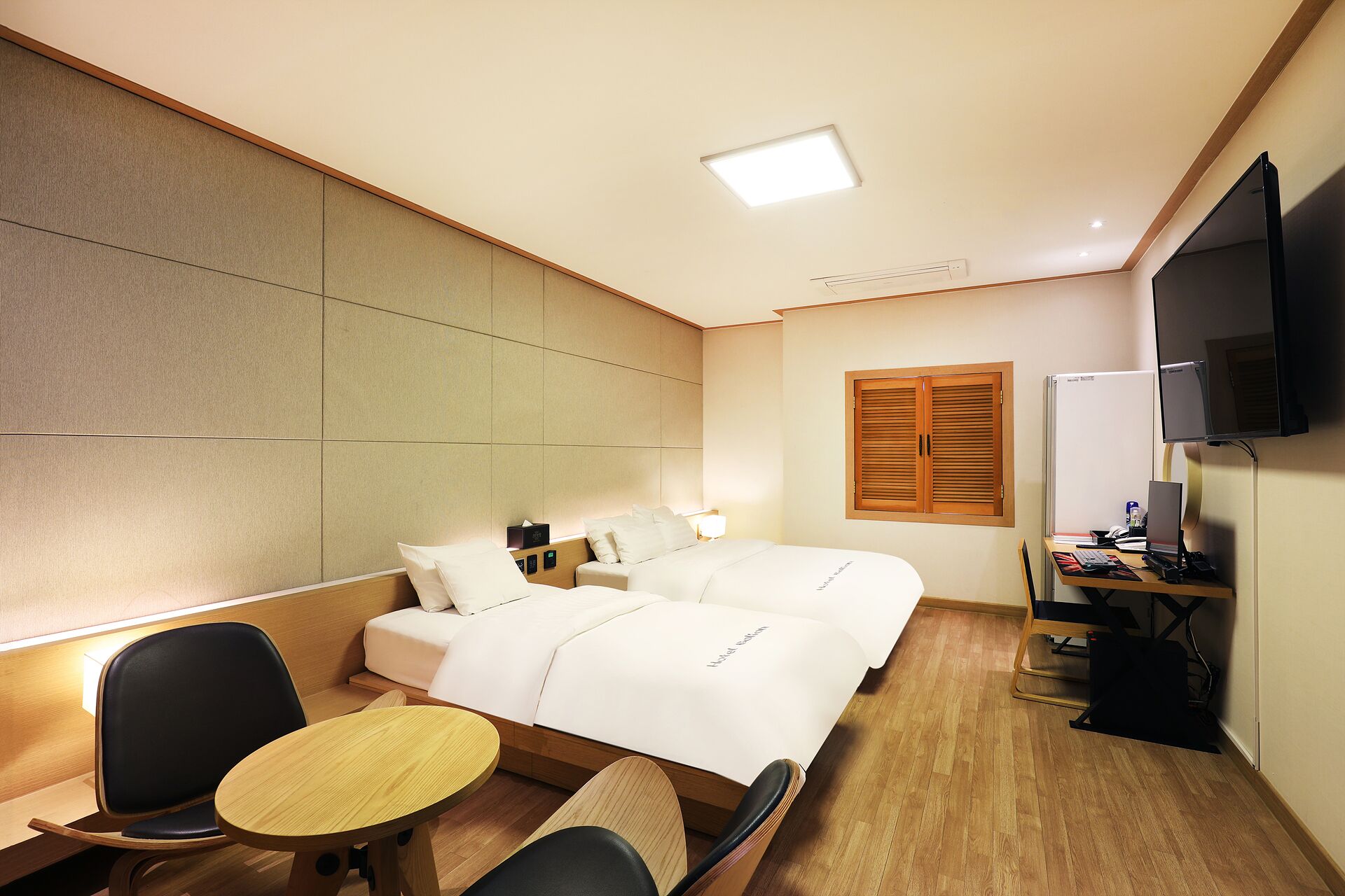 A hotel room with two beds, a desk, a chair, a TV, and a window with blinds.