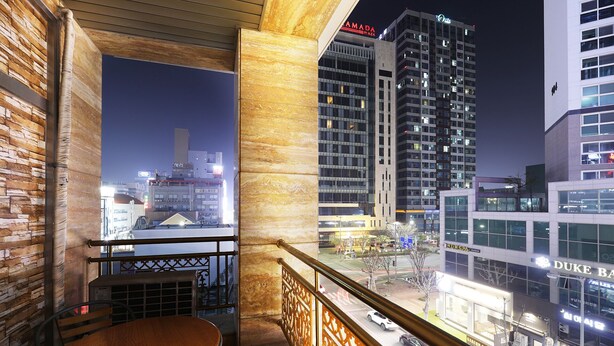 A balcony with a wooden table and chairs, overlooking a cityscape at night with illuminated buildings and a clear view of the street below. - Bolton Hotel (Gwangju)